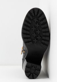 Stivale alla caviglia nero con tomaia in pelle texturizzata, suola in gomma robusta con profonde scanalature e zip laterale con ferramenta dorata.
