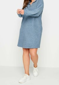 Robe zippée en polaire bleue avec manches longues, col montant et coupe décontractée, associée à des baskets blanches. Texture lisse et longueur genou.