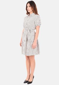 Abito a righe con bottoni, maniche corte a palloncino, annodato in vita e design della gonna a strati. Colori: bianco e nero.