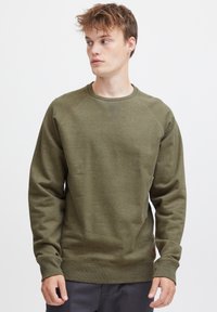 Pulover de culoare verde măsliniu, cu guler rotund striat, mâneci lungi și un finisaj texturat. Are o eticheta mică cu logo pe partea inferioară.