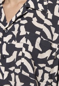 Camicia a maniche corte realizzata in tessuto leggero, con un motivo astratto nero e crema, colletto a contrasto e taschino sul petto con marchio.