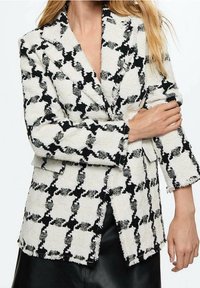 Blazer a rayas en blanco y negro, hecho de una tela texturizada, con cuello de muesca y bordes ligeramente deshilachados.