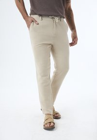 Beige Baumwollmischungshosen mit einem Kordelzugbund, schlankem Schnitt, glatter Textur und Seitentaschen, kombiniert mit braunen Sandalen.
