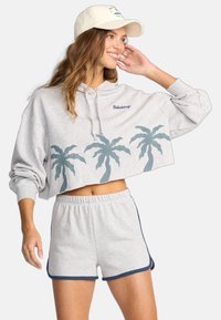 Lichtgrijze cropped hoodie met palmbomenontwerpen langs de onderkant en blauwe accenten. Gecombineerd met bijpassende grijze shorts met een blauwe rand.