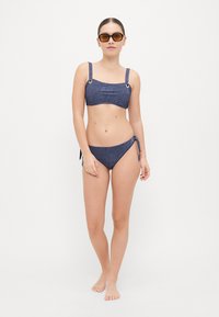 Denim-stijl bikini met een bandeau-top voorzien van metalen ringen op de bandjes en een verstelbare zijstrik-bodem, beide in donkerblauw.
