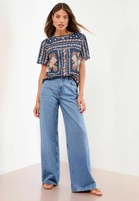 Haut en imprimé floral marine avec des manches courtes à volants, associé à un jean large à taille haute en denim clair et des sandales plates marron.