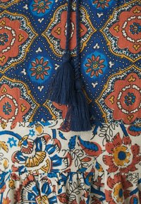 Abito multicolore con un motivo floreale blu, rosso e giallo, completo di una cravatta blu navy e nappine. Il tessuto è di cotone texturizzato con un design a strati.
