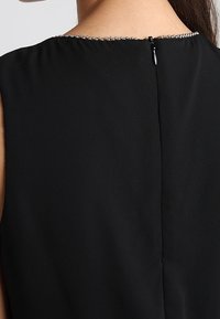 Svart ärmlös klänning med en mjuk textur, med en pärlkrage och en liten dragkedjestängning på baksidan.