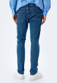 Jeans de mezclilla azul ajustados con una textura descolorida, diseño de cinco bolsillos y un ligero estiramiento. Presentan una cintura media y un corte a la altura del tobillo.