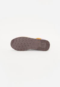 Semelle de sneaker en caoutchouc brun texturé, avec une adhérence à motifs et un talon arrondi. Des accents multicolores sur les côtés rehaussent le design.