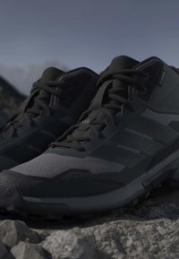 Ζευγάρι μαύρα και γκρι παπούτσια πεζοπορίας με κορδόνια που ακουμπούν σε βραχώδη περιοχή κάτω από καθαρό ουρανό.