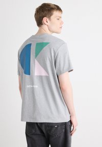 Grå bomulds t-shirt med et stort abstrakt design i blå, grøn og pink på ryggen. "Calvin Klein" logo i hvid under designet.