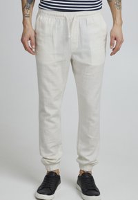 Joggers de lino color beige claro con cintura elástica, cierre con cordón y puños elásticos. Combinados con zapatillas negras.