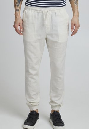 Light beige linen joggers with an elastic waistband, drawstring closure, and elastic cuffs. Paired with black sneakers.