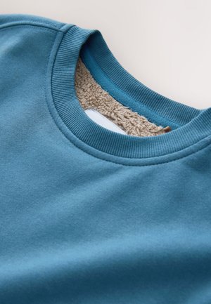 Sudadera azul con cuello redondo acanalado y forro interior suave y texturizado. Presenta tela lisa con un forro interior en color crema contrastante.