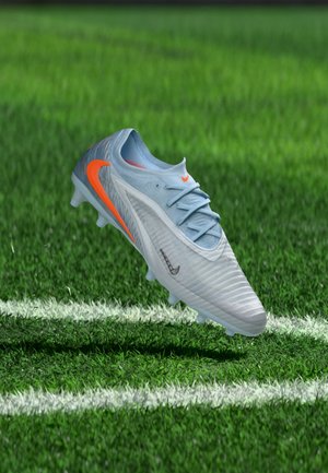 Une chaussure de football Nike bleu clair aux accents orange flotte au-dessus d’un terrain vert et franchit une ligne de touche blanche.