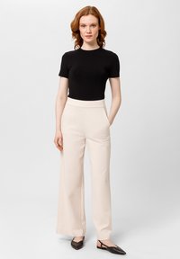 Czarna dopasowana koszulka, beżowe spodnie z wysokim stanem i szerokimi nogawkami, gładka faktura, kieszenie boczne, w zestawieniu z ciemnobrązowymi butami na obcasie typu slingback.