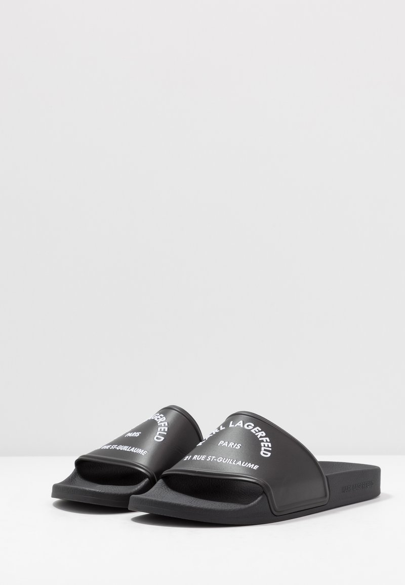 Chaussons de plage noirs avec une surface en caoutchouc lisse, présentant un texte blanc en relief sur les brides. Le texte inclut "Karl Lagerfeld" et "Paris."