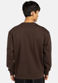 Felpa marrone con scollo rotondo e maniche lunghe. Tessuto liscio con polsini e fondo a coste, caratterizzata da una vestibilità comoda e senza loghi visibili.