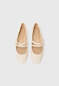 Cream patent leather ballet flats with rounded toes, two narrow straps across the instep, and decorative buttons on each strap.