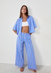 Jasnoniebieska, w paski koszula z krótkim rękawem z białymi i czerwonymi wzorami, w połączeniu z szerokimi spodniami w tym samym kolorze. Miękka tkanina z elastycznym pasem.