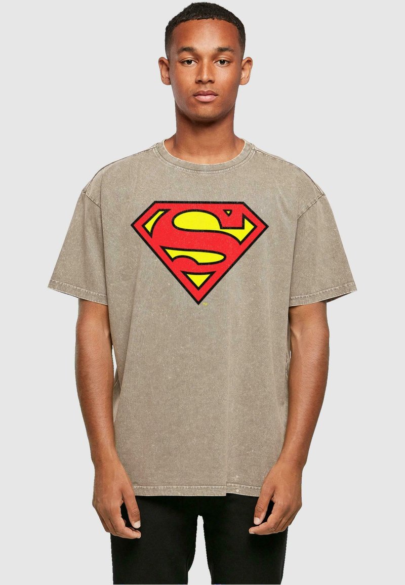 Camiseta de algodón beige con un gran logo de Superman en rojo y amarillo en el pecho, con mangas cortas y escote redondo.