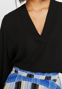 Black blouse with a V-neck, paired with a skirt featuring a multicolored striped pattern in blue, black, and beige.