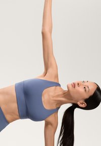 Svetlomodrá športová podprsenka s výstrihom do polkruhu v kombinácii s ladnými legínami. Hladká textura, navrhnutá na aktívny pohyb.