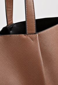 Gros plan sur un sac cabas en cuir texturé marron avec des poignées cousues et une doublure intérieure noire.
