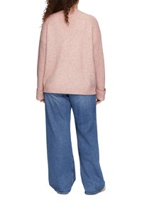Jasnoróżowy sweter z dzianiny o luźnym kroju, z opadającymi ramionami i ściągaczami, zestawiony z szerokimi dżinsami w niebieskim kolorze.