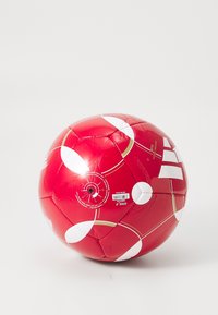 Rød fodbold med hvide og gyldne geometriske mønstre, delvist deflateret, vist mod en ensfarvet hvid baggrund.