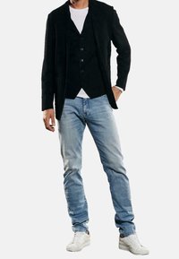 Czarna marynarka na czarnej kamizelce, w połączeniu z białym t-shirtem, jasnoniebieskimi jeansami i białymi tenisówkami. Miękkie tekstury i dopasowany krój.
