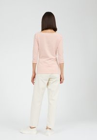 Stribet langærmet skjorte i lys pink og hvid, afslappet fit, parret med cremefarvede bukser og hvide sneakers, taget bagfra.