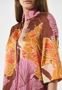 Brunblommig blus med hög krage, med orange och rosa nyanser, mjuk satintextur och 3/4-lång ärm.