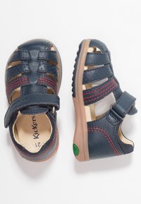 Sandalias de cuero azul marino con costuras rojas, diseño abierto, cinta de Velcro y suela de goma con un acento verde. Ideales para la comodidad y la transpirabilidad.