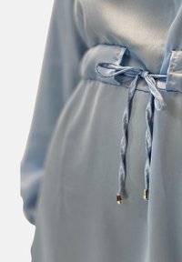 Lyseblå satinbeklædning med et bundet bælte med silkebløde snore og metalliske ender, glat tekstur og et flydende design.