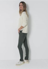 Krämfärgad ribbad tröja, åtsittande olivgröna byxor och vita sneakers. Outfiten har en avslappnad design och en mjuk textur.