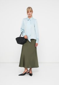 Blusa de seda azul clara com detalhe de laço, saia satin verde e bolsa preta. Design ajustado, textura suave e sapatos de salto pretos com bico.
