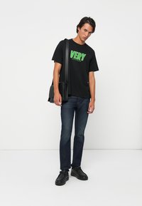 Čierne bavlnené tričko s green "VERY" textom a detailom "CALVIN KLEIN", spárované s tmavomodrými džínsami a čiernymi teniskami.