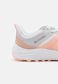 Zapatilla de running ligera con parte superior de malla transpirable en gris, durazno y blanco. Acentuada con cordones en tonos pastel y una suela exterior texturizada.