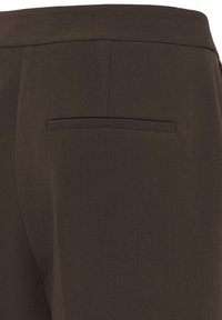 Gros plan sur un pantalon marron foncé sur mesure montrant une seule poche passepoilée au dos et des coutures à la ceinture.