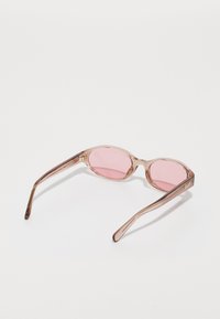 Lunettes de soleil ovales roses claires avec une monture transparente, présentant un léger marquage sur le côté et des branches légèrement courbées pour plus de confort.