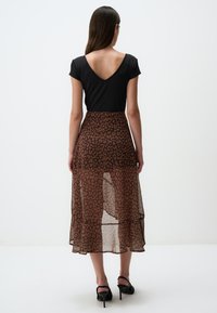 Haut noir à manches courtes avec un dos en V profond, associé à une jupe marron semi-transparente ornée d'un imprimé léopard et d'un ourlet évasé.