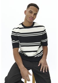 Pull à rayures noires et blanches à manches courtes avec une texture côtelée et un col rond ; associé à un pantalon sombre.