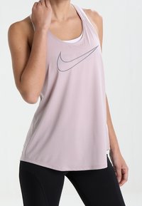 Różowy stanik sportowy wykonany z lekkiego materiału, z szarym logo Nike, designem na plecach w stylu racerback i luźnym krojem.