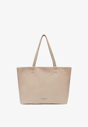 Beżowa skórzana torba tote z dwoma długimi uchwytami, gładką teksturą, minimalnymi detalami przeszycia oraz wytłoczonym logo marki na dole.