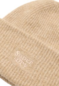 Beige wollen beanie met een ribbeltextuur. Voorzien van een geborduurd "Super Dry" logo in lichtroze. Platte en strakke pasvorm.