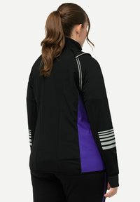 Sort og lilla atletisk jakke med høj krave, sidelapper og reflekterende striber på ærmerne. Glat tekstur, tætsiddende design.