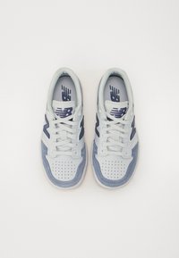 Hvite og lyseblå sneakers laget av semsket skinn og mesh-materialer, med perforert tåboks, snøredesign og dristige marineblå logo-detajer.