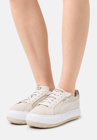 Baskets en suède beige avec une semelle blanche épaisse, design à lacets et logo PUMA sur la languette et le côté. Accents texturés sur la semelle.